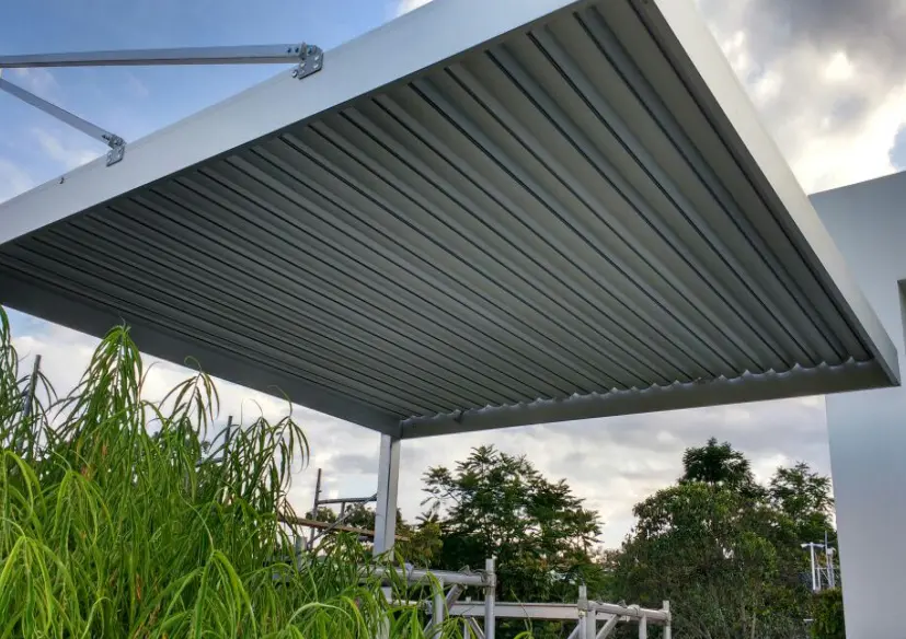 White aluminum pergola shelters an outdoor space in a garden